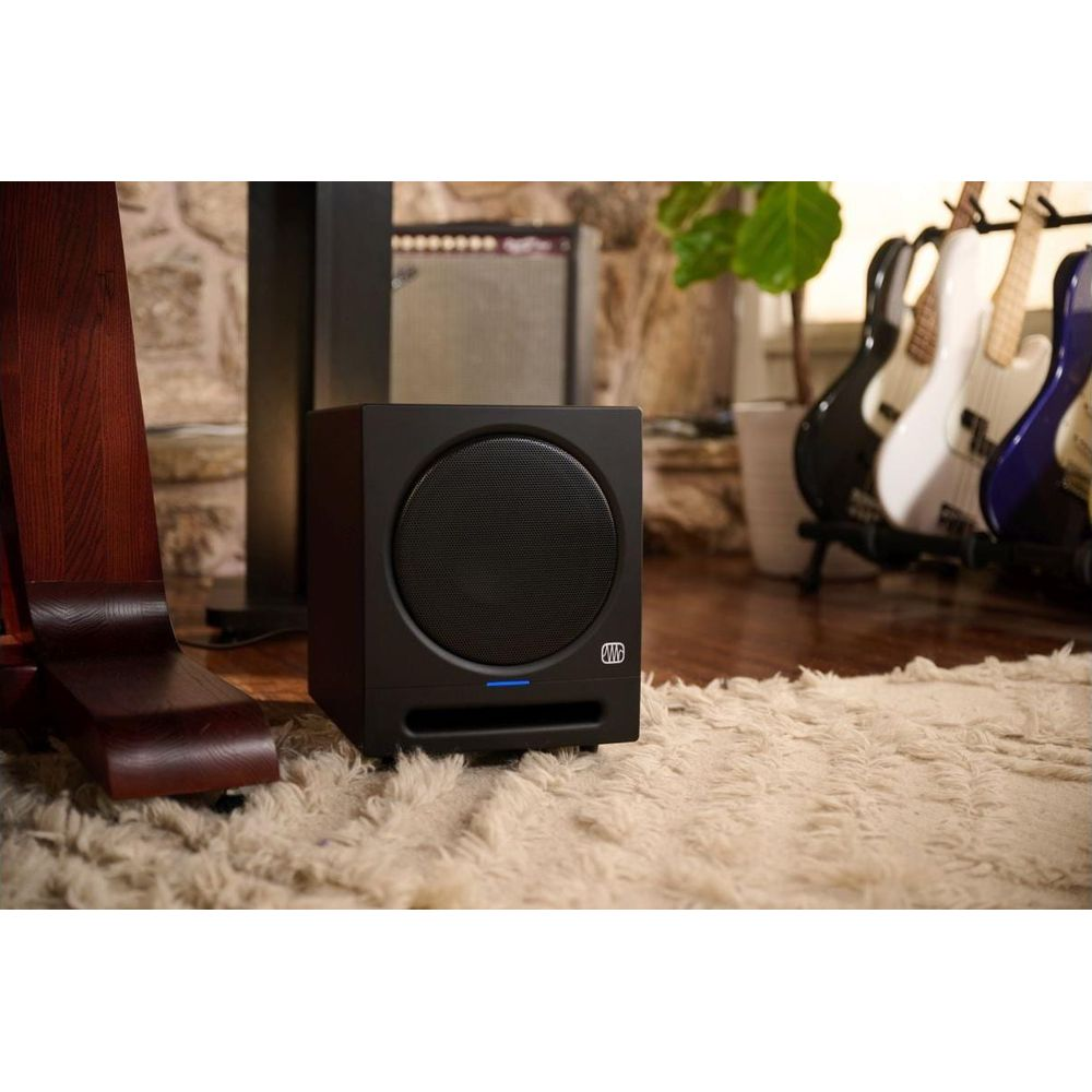 Un subwoofer nero su un tappeto chiaro, con chitarre elettriche nelle vicinanze.