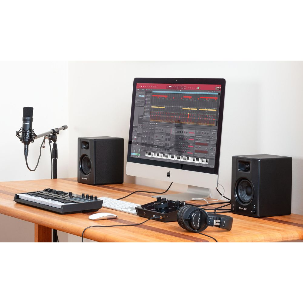 Ein Desktop-Computer mit Musikproduktionssoftware, Lautsprechern, Mikrofon, Tastatur und Kopfhörern auf einem Holztisch.