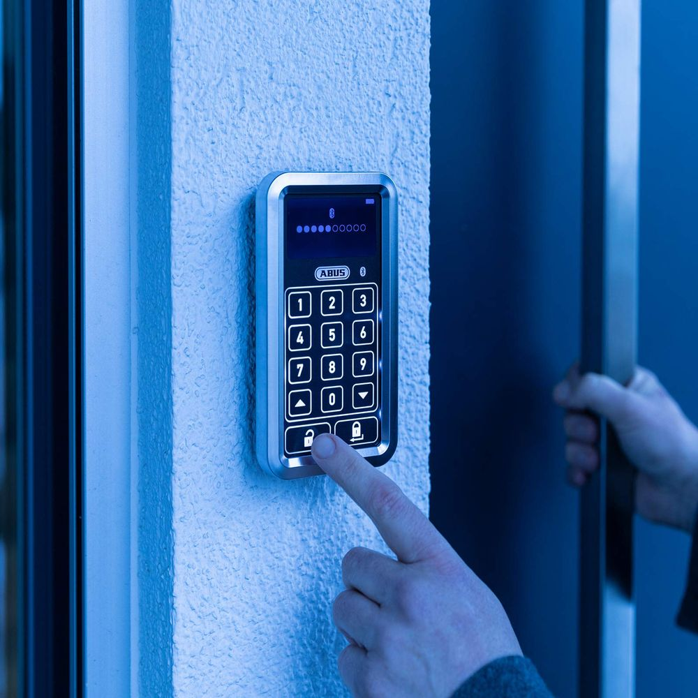 Ein Finger drückt auf die Entriegeltaste eines beleuchteten Zahlenschlosses.
