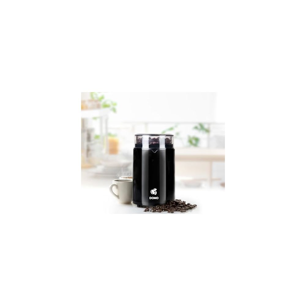 Molinillo de café negro con granos de café y una taza al fondo.
