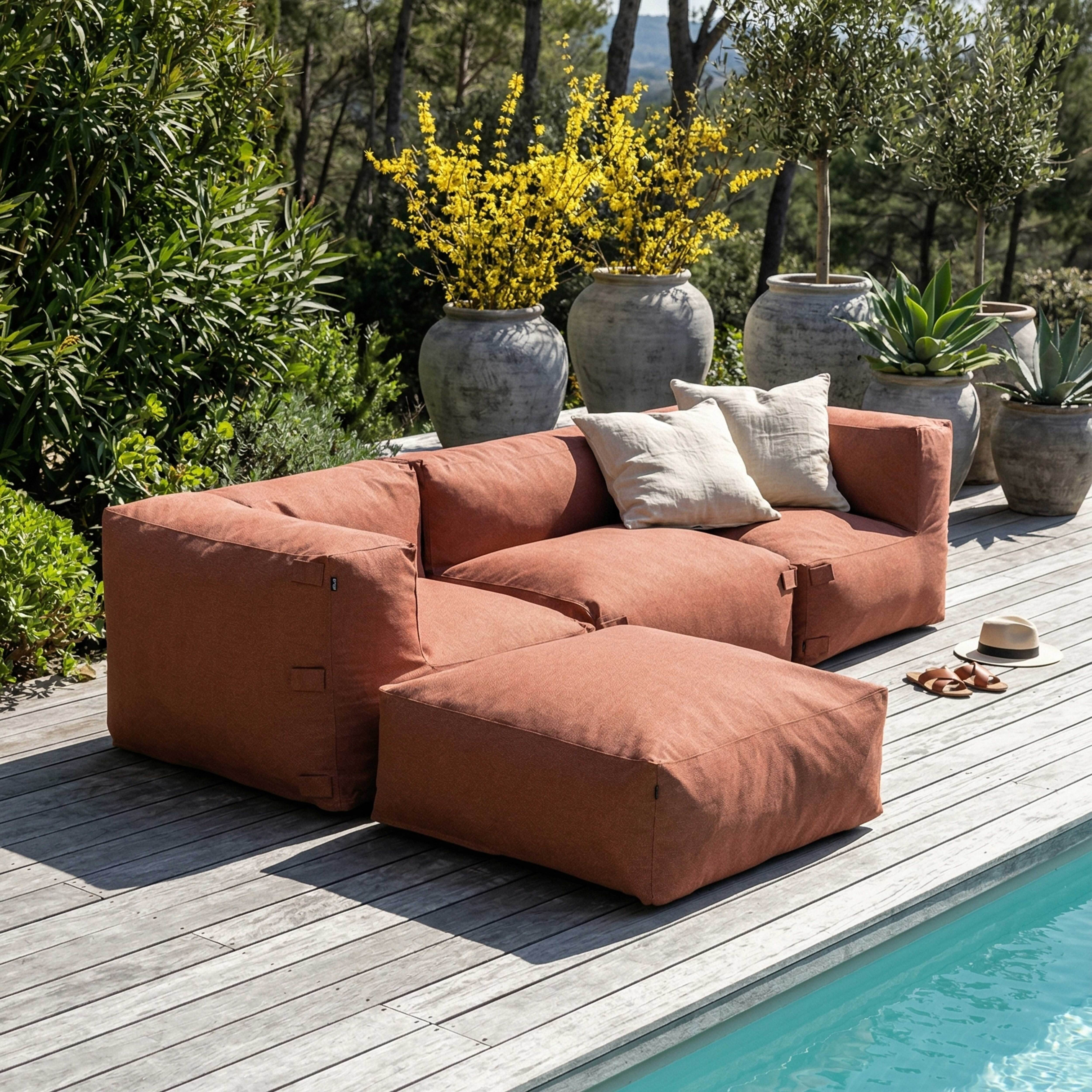 Ein orangefarbenes Modulsofa mit Kissen steht auf einer Holzterrasse am Pool.