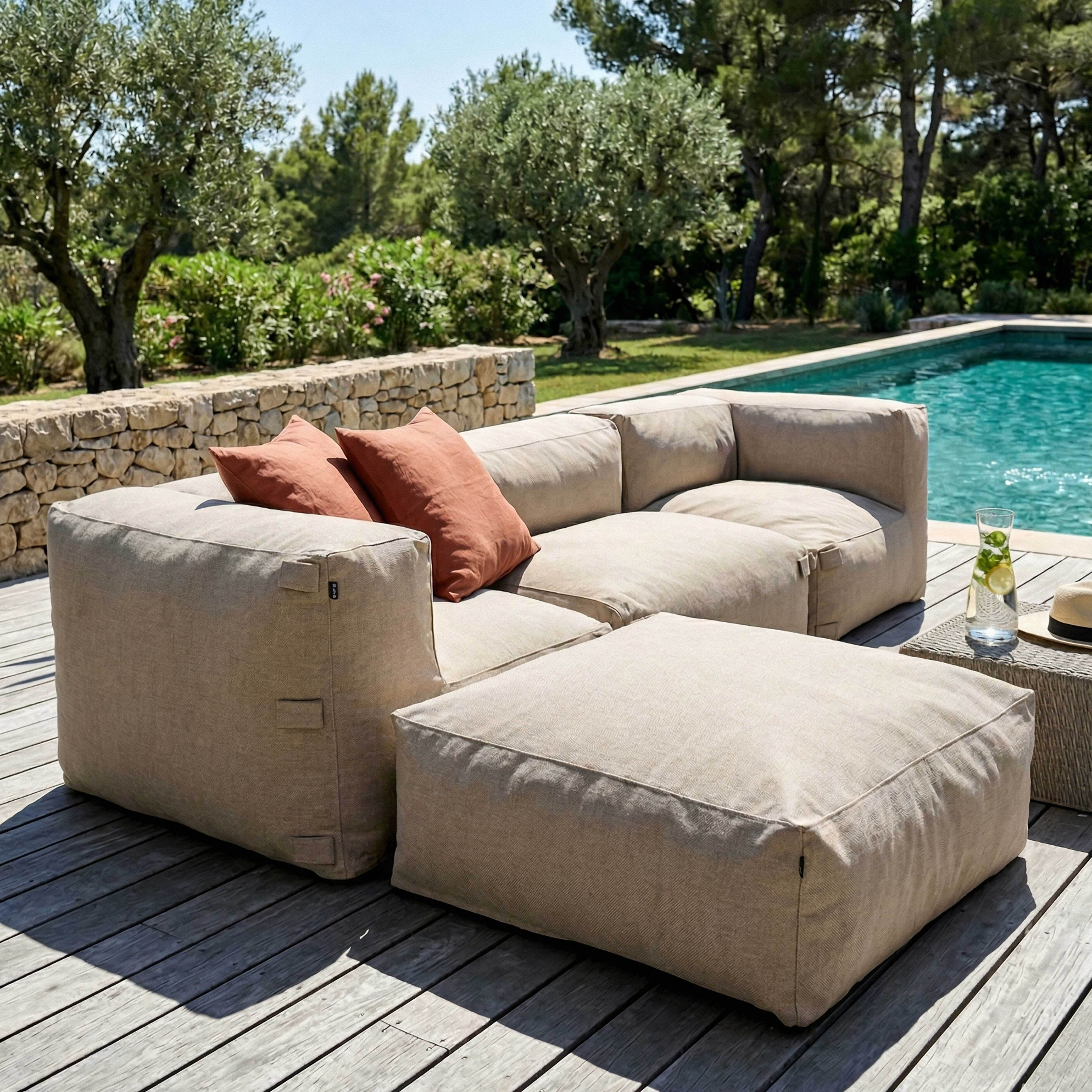 Ein beiges Lounge-Sofa mit zwei orangen Kissen neben einem Pool.