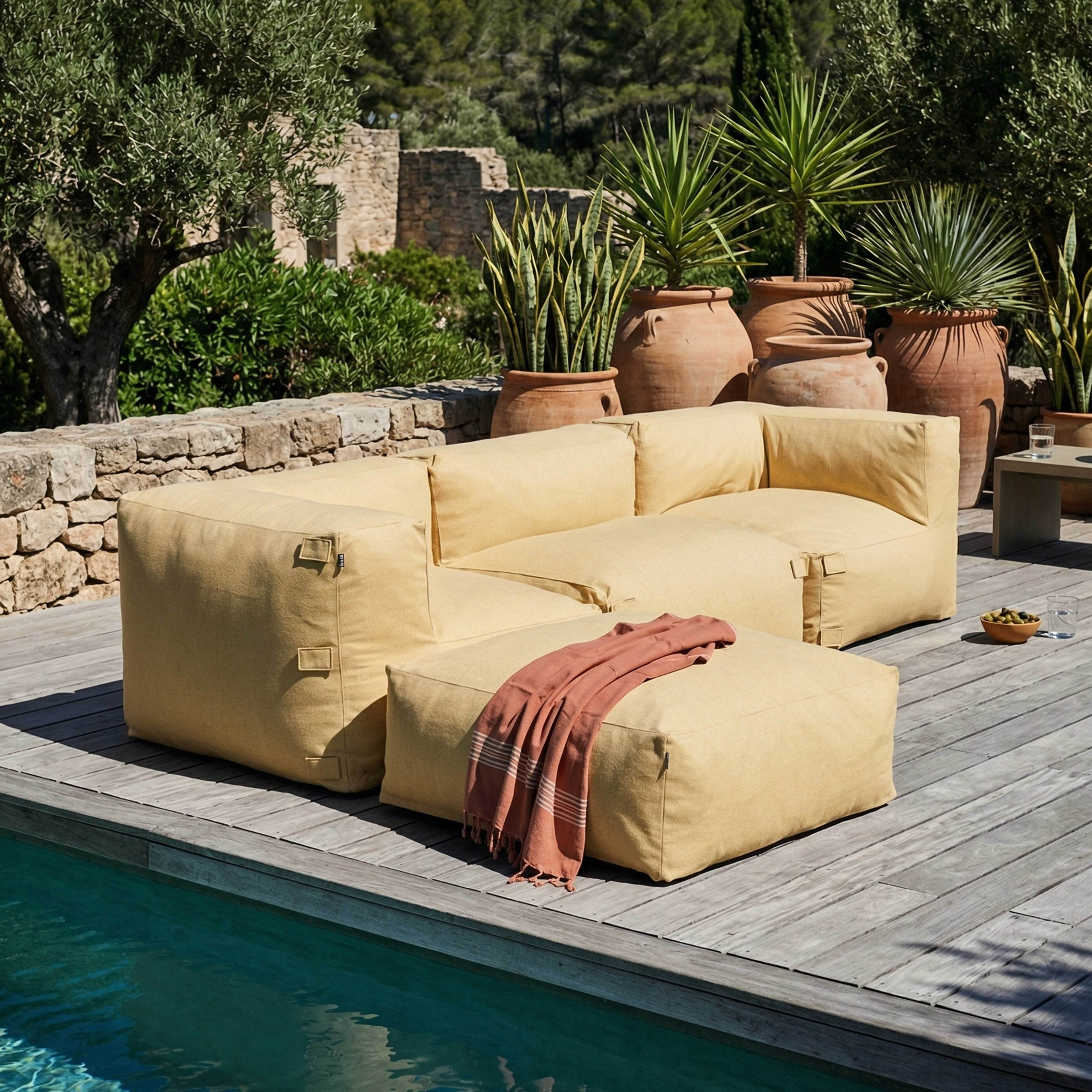 Gelbe Lounge-Möbel am Pool mit Terracotta-Töpfen und Pflanzen im Hintergrund.