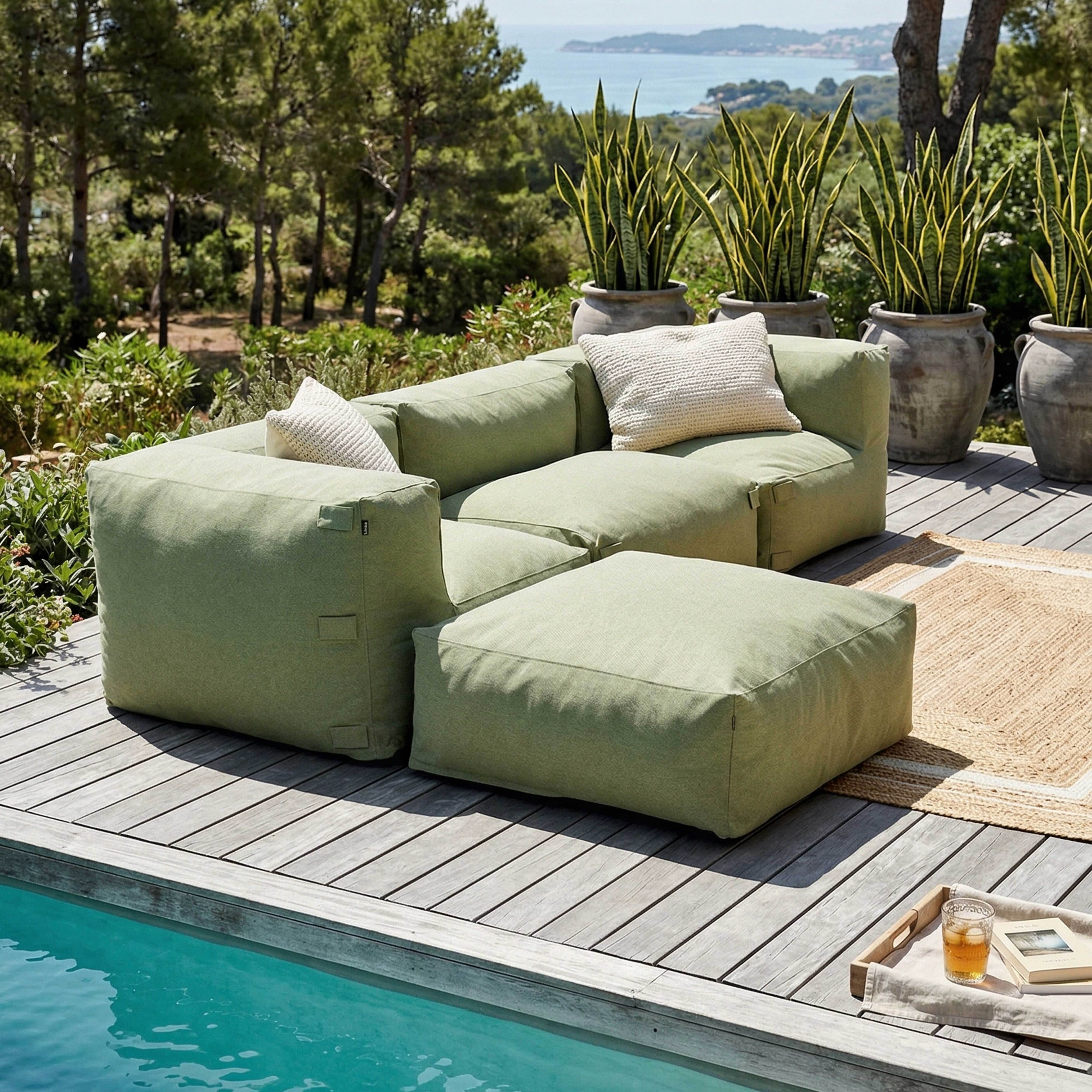 Grünes Lounge-Set auf Holzdeck mit Pool und Meerblick.