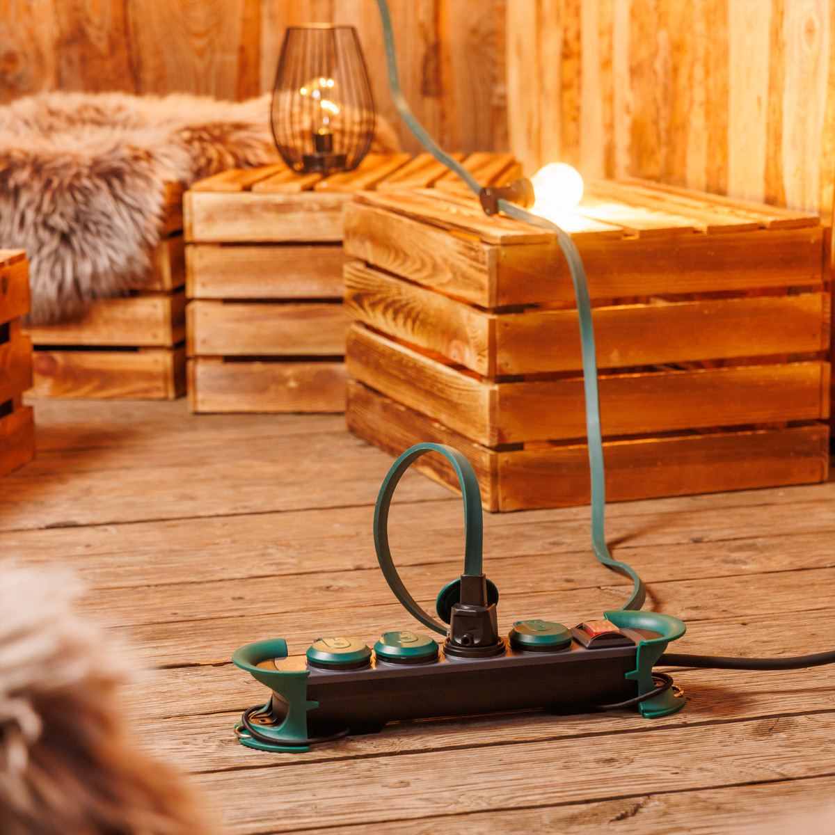 Eine schwarze Steckdosenleiste mit grünen Akzenten steht auf einem Holzboden und ist mit einer Lichterkette verbunden.