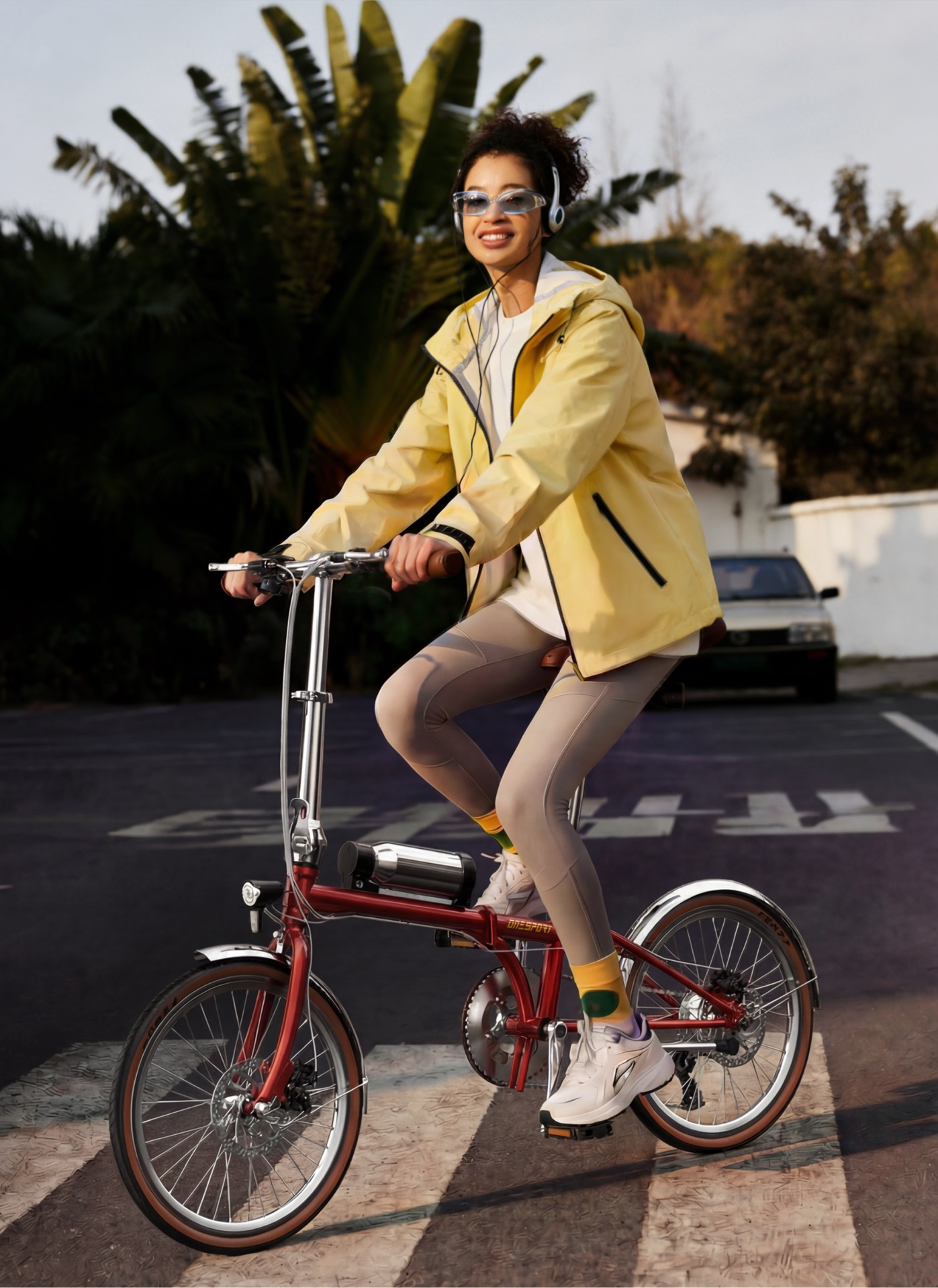 Una donna in giallo guida una bicicletta rossa, indossa cuffie e occhiali da sole.