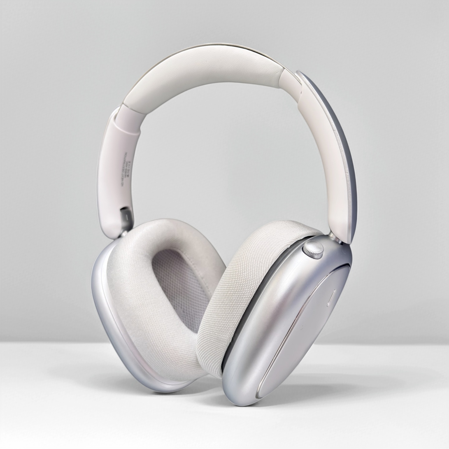 Auriculares plateados con diadema y almohadillas blancas sobre superficie blanca.