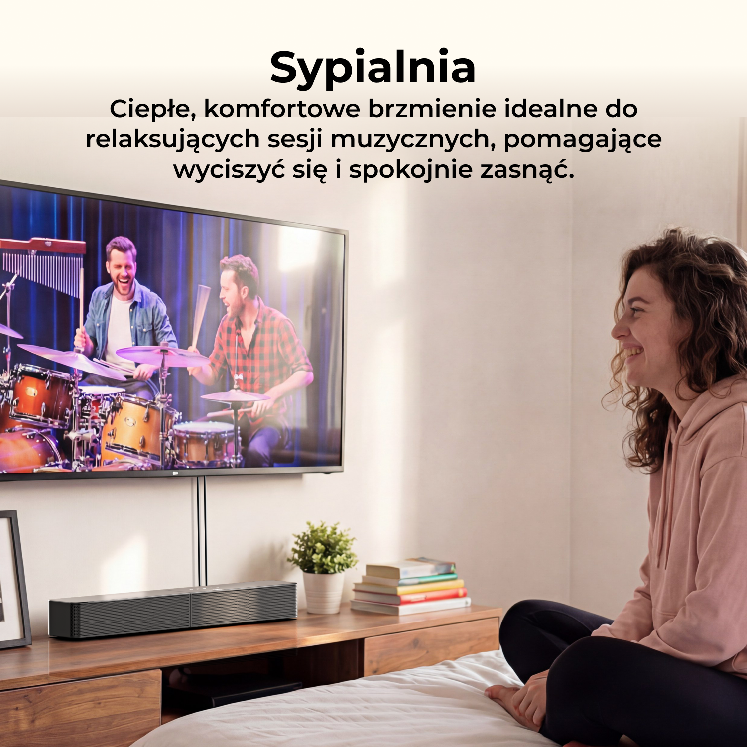 Kobieta siedzi na łóżku, uśmiecha się, oglądając dwóch mężczyzn grających na perkusji na ekranie telewizora z soundbarem pod spodem.