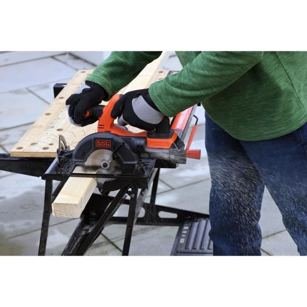 Osoba w rękawiczkach tnie drewno piłą tarczową na ławce warsztatowej.