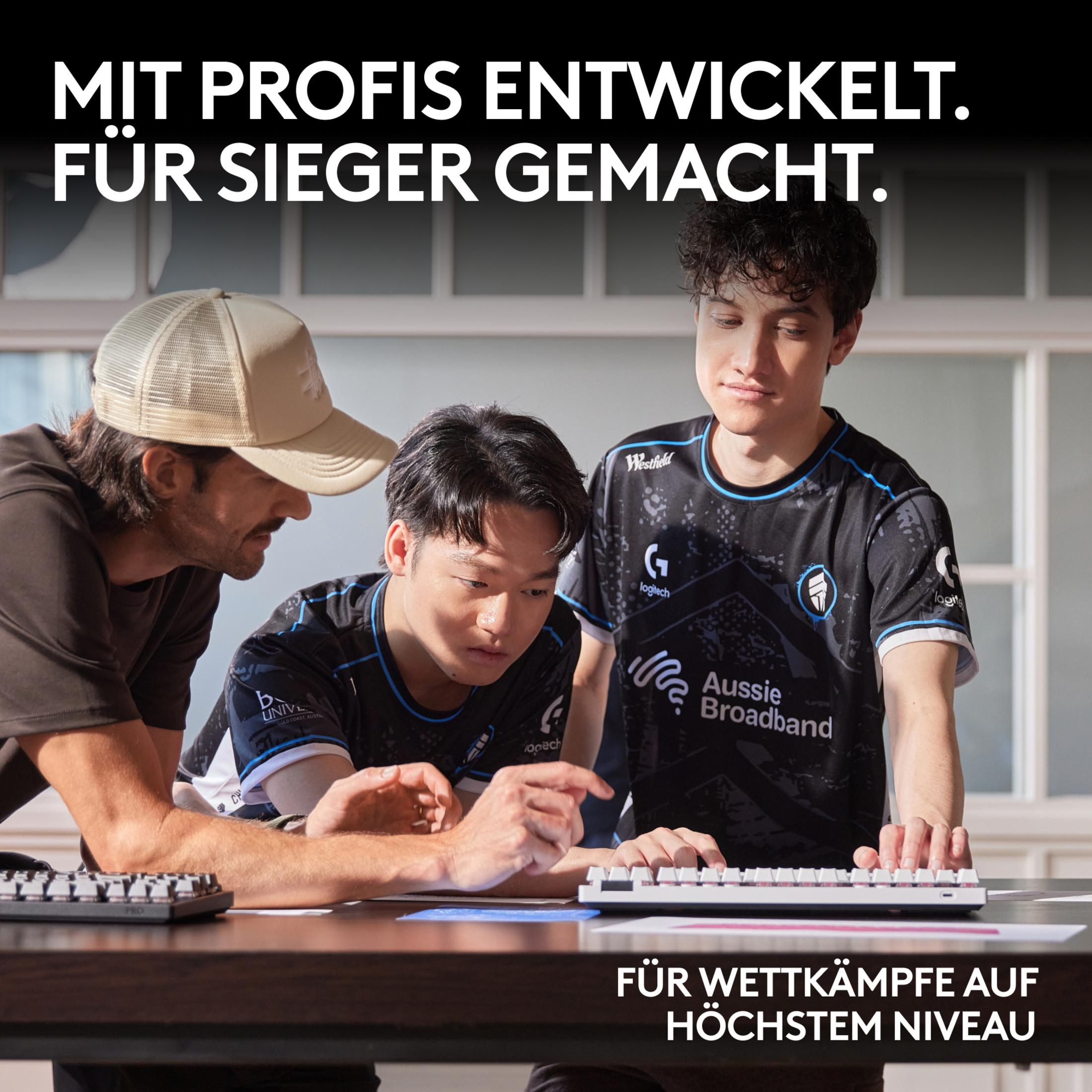 Trzech młodych mężczyzn w koszulkach e-sportowych patrzy na klawiaturę. Jeden na nią wskazuje.