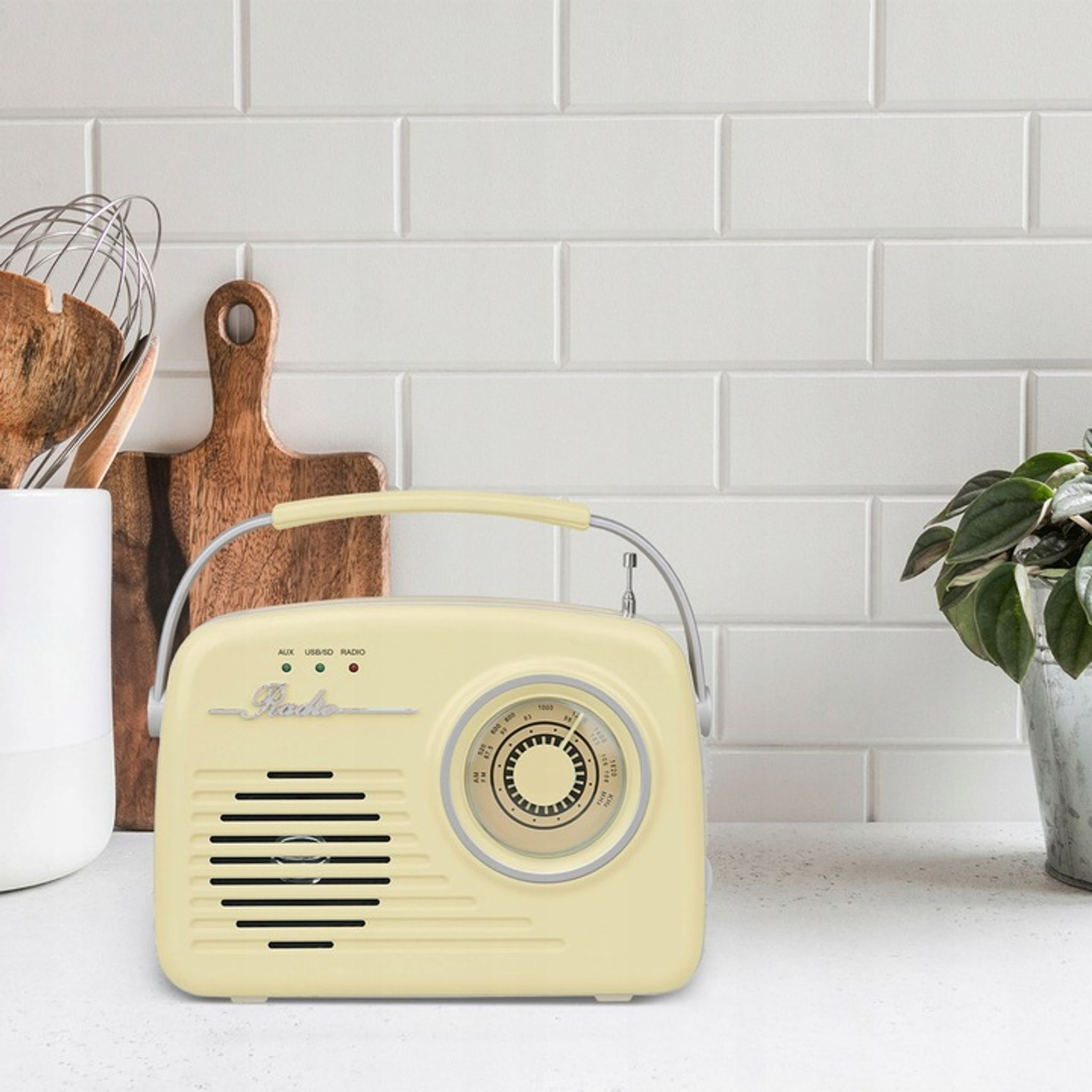 Żółte radio w stylu retro stoi na blacie kuchennym na tle białych płytek metra.