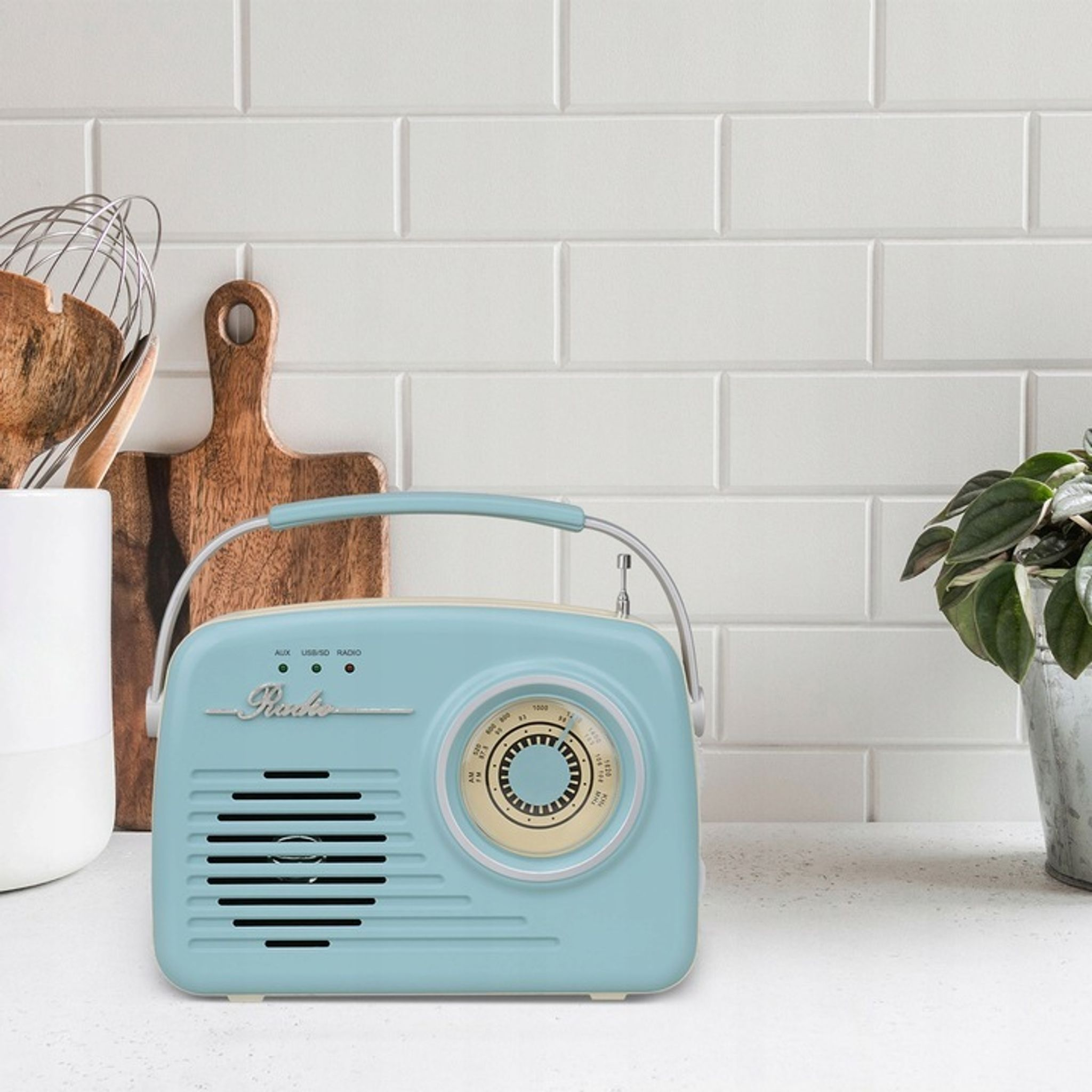 Jasnoniebieskie radio retro na białym blacie obok deski do krojenia i garnka.