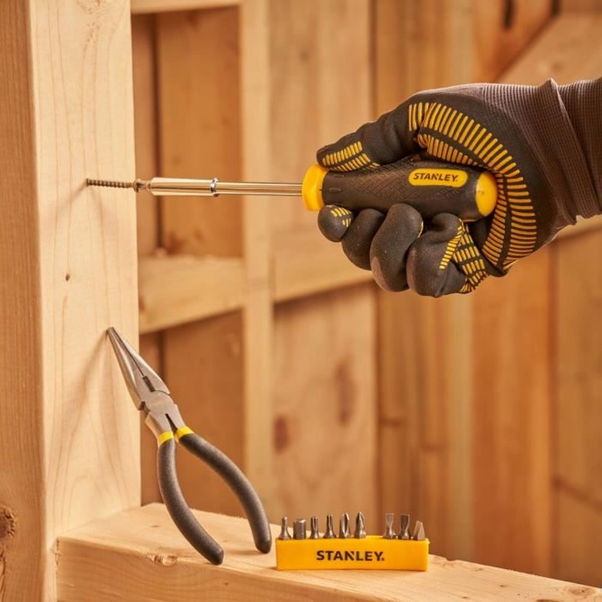 Ręka w rękawicy wkręca śrubę w drewno. W pobliżu kombinerki i bity.