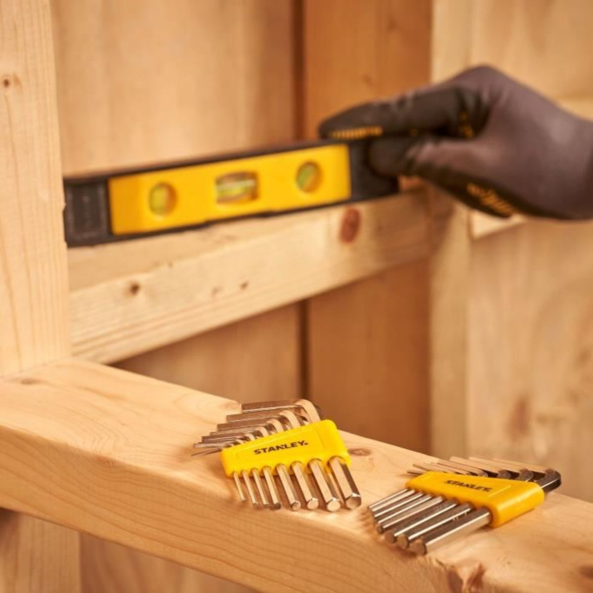 Żółta poziomica na drewnie. Obok leżą dwa zestawy kluczy imbusowych.