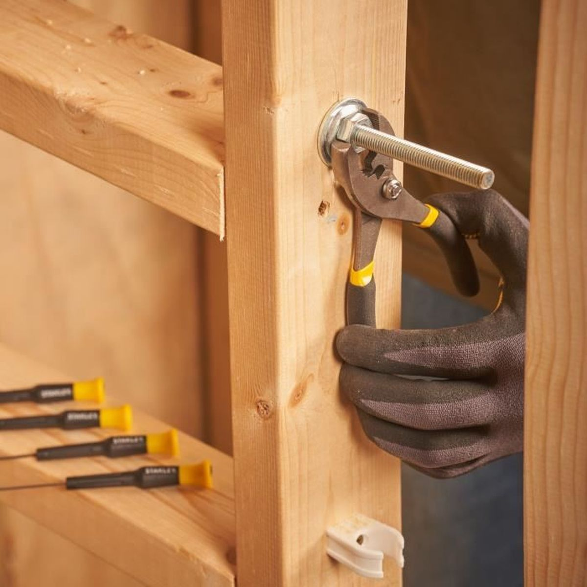 Narzędzie trzyma śrubę na drewnianym słupku, osoba w rękawicy.