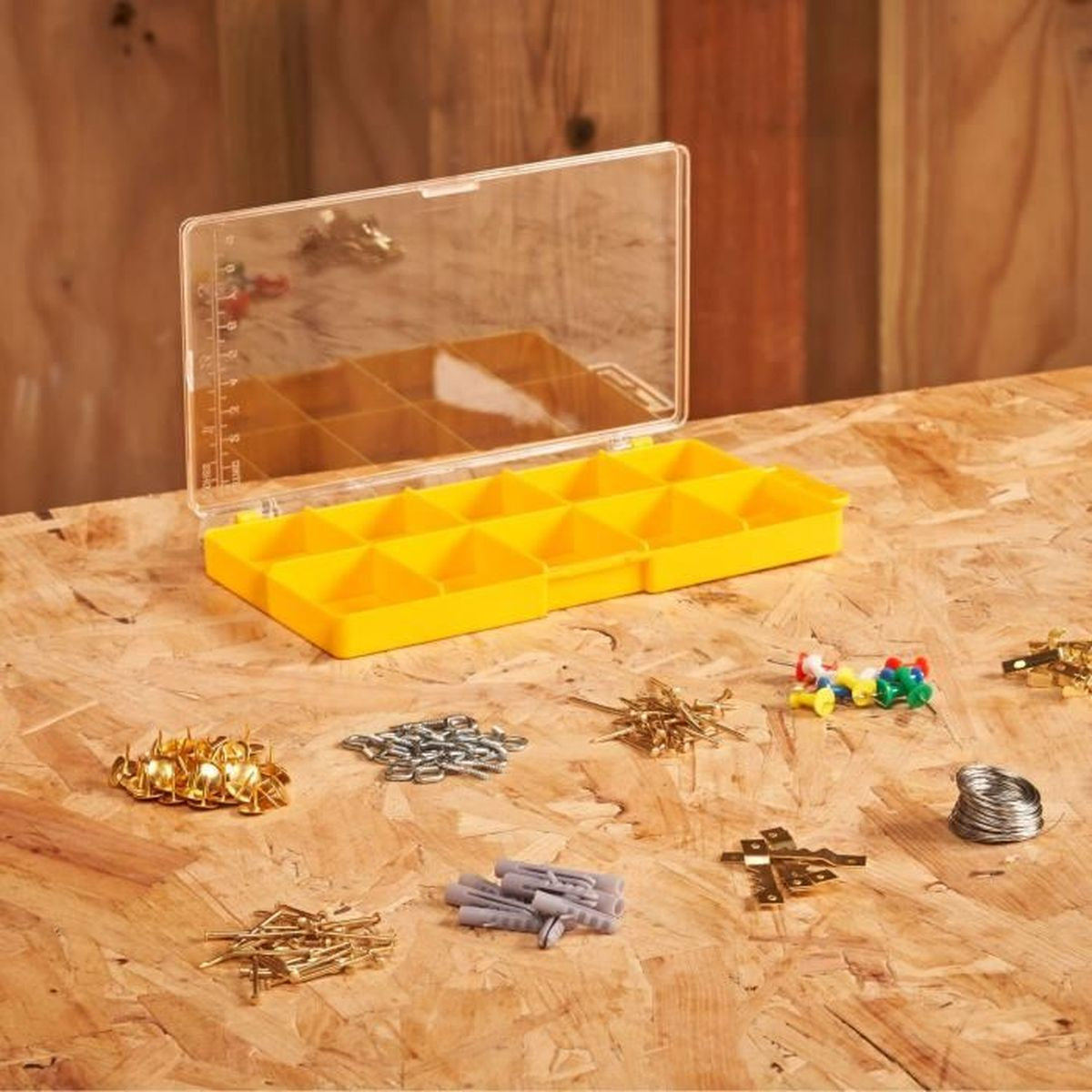 Otwarty żółty organizer z różnymi śrubami, gwoździami i kołkami na drewnie.