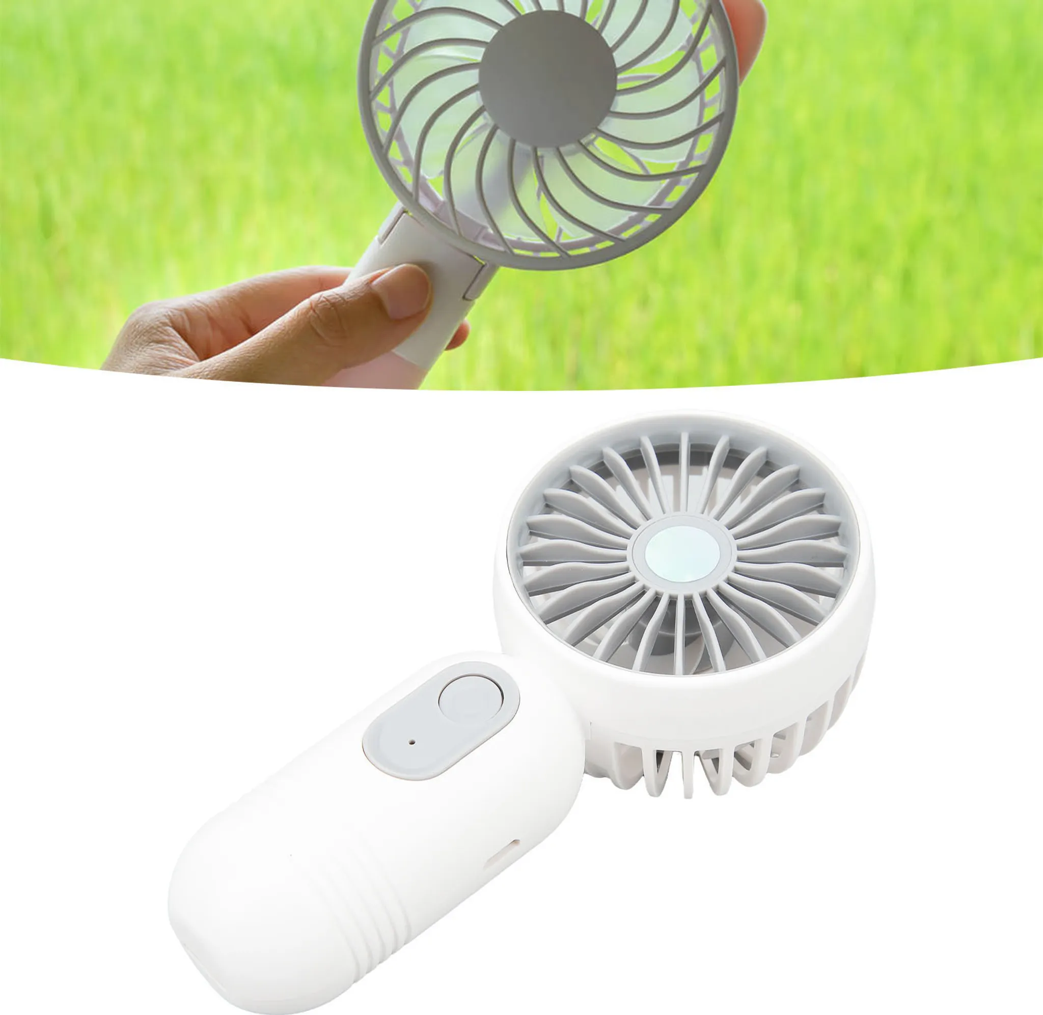 Eine Hand hält einen weißen Handventilator mit grauen Lüfterblättern vor grünem Gras.