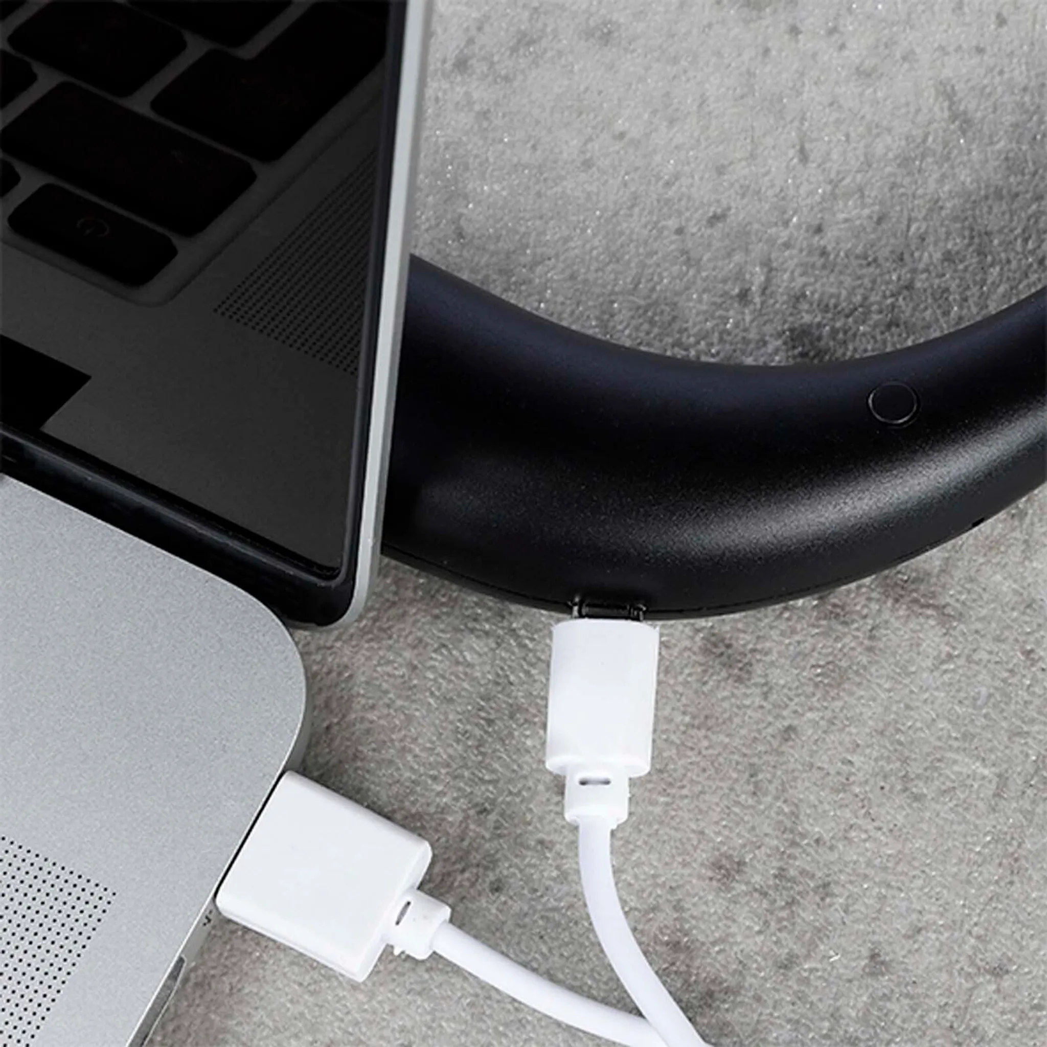 Ein weißes USB-Kabel wird in einen Laptop und ein schwarzes Gerät gesteckt.
