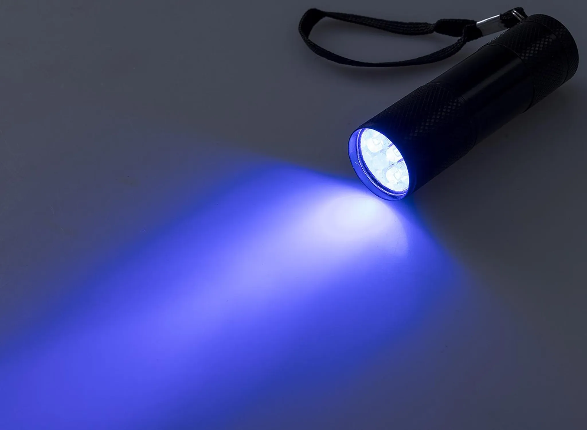 Ein schwarzer UV-Strahler mit blauem Lichtkegel auf einem grauen Untergrund.