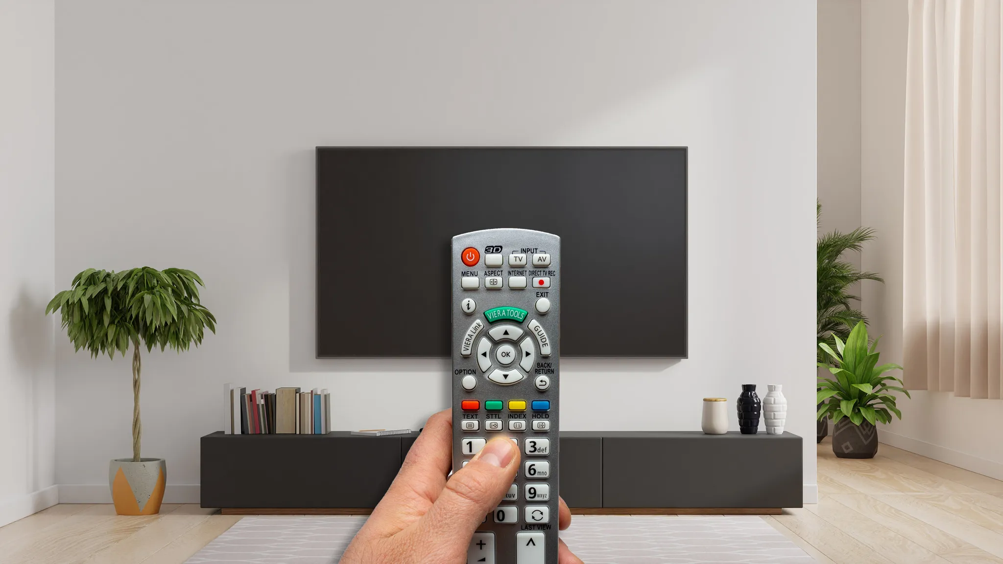 Eine Hand hält eine silberne TV-Fernbedienung vor einem dunklen Fernsehbildschirm.