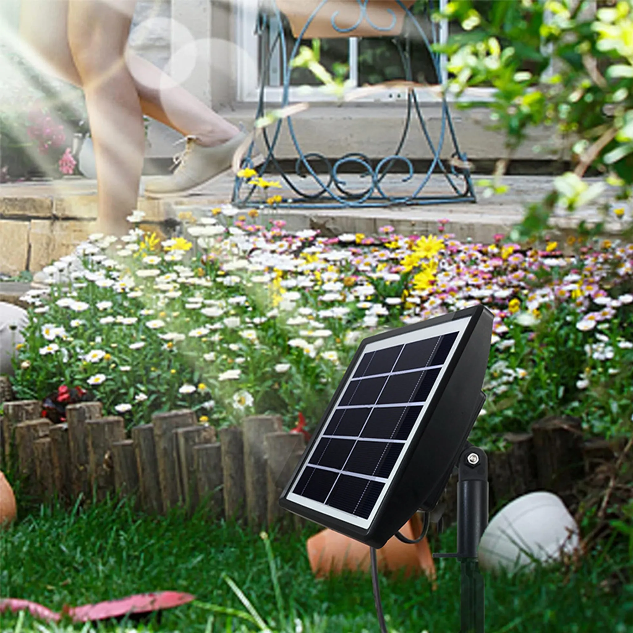 Ein Solarpanel steht in einem Garten mit den Beinen einer Person und einem Blumenbeet.
