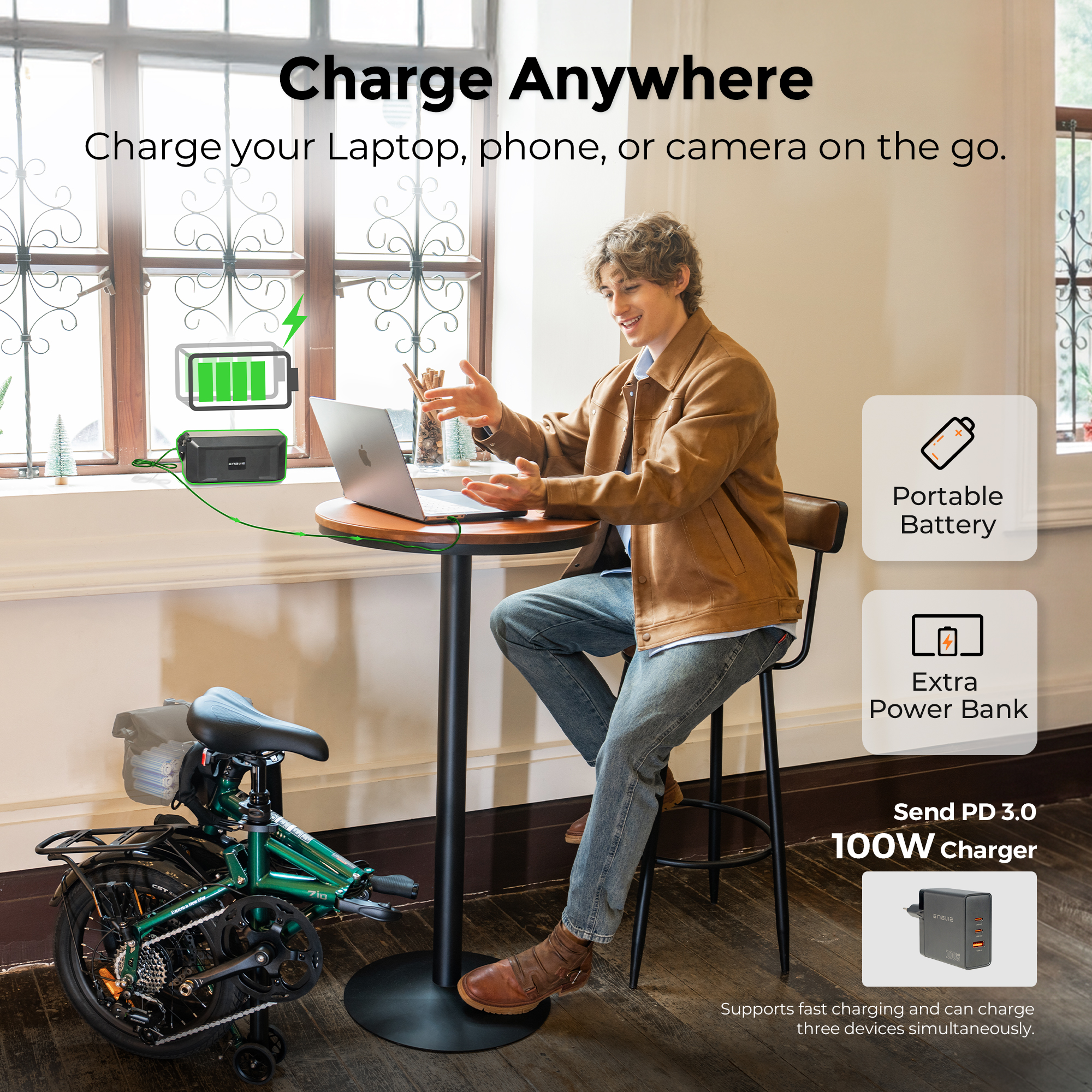 Uomo seduto al tavolo, carica laptop con power bank. Bicicletta verde nelle vicinanze.
