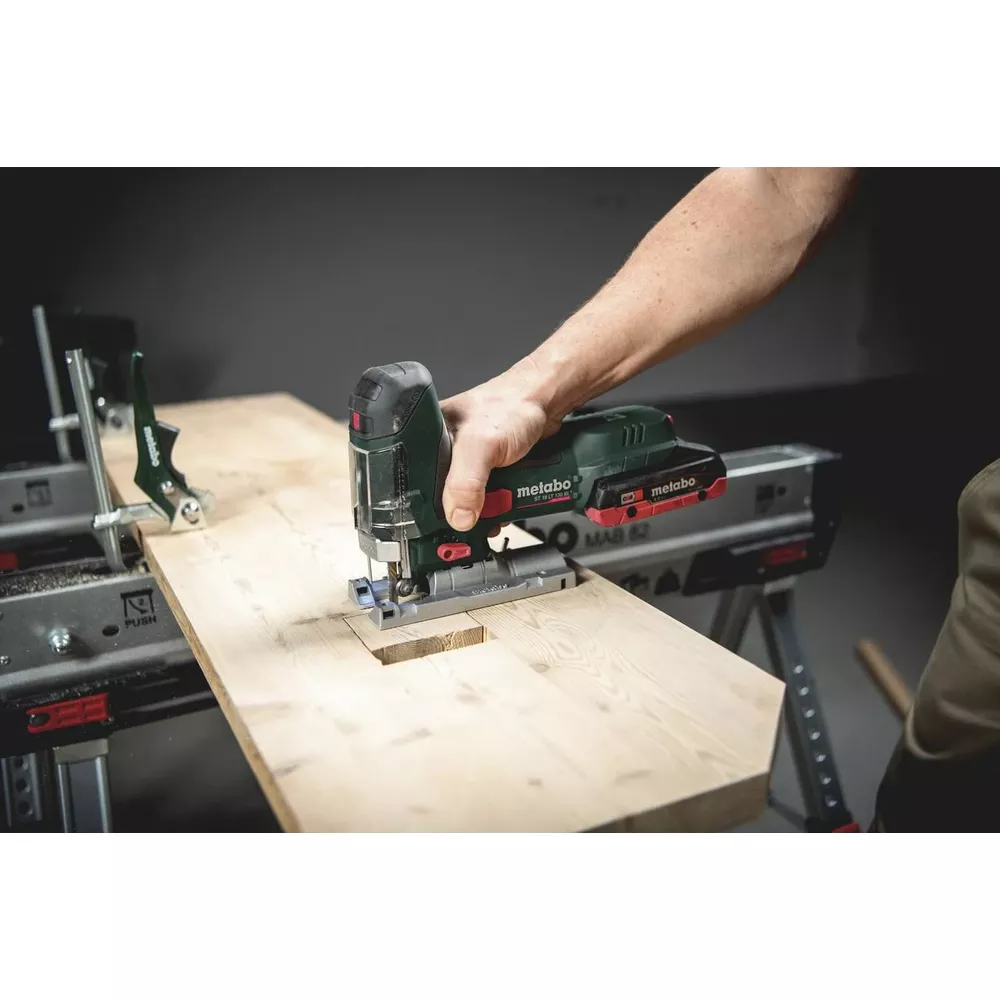 Green jigsaw cutting a hole in a wooden board, held by hand.