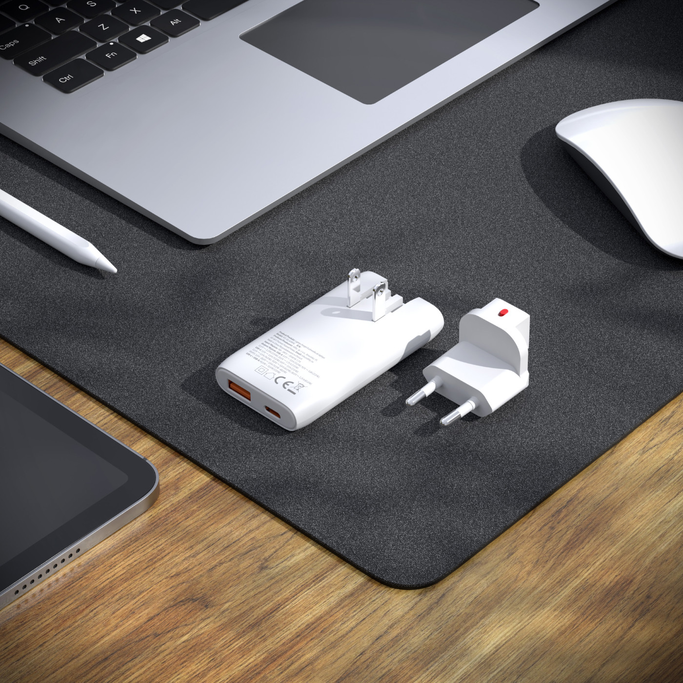 Biały adapter podróżny obok laptopa, myszy i tabletu.