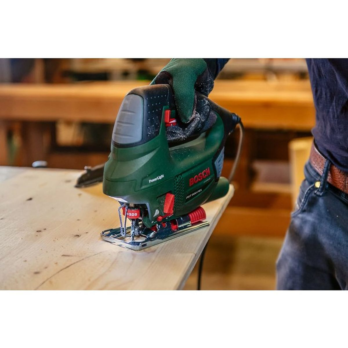 Zielona wyrzynarka Bosch na desce, trzymana ręcznie, warsztat w tle.