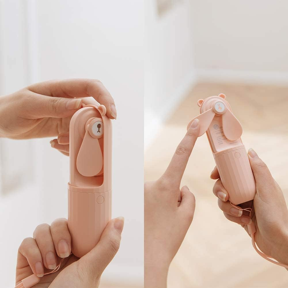 Hände halten einen rosa bärenförmigen Ventilator. Eine Hand öffnet ihn, die andere drückt einen Knopf.