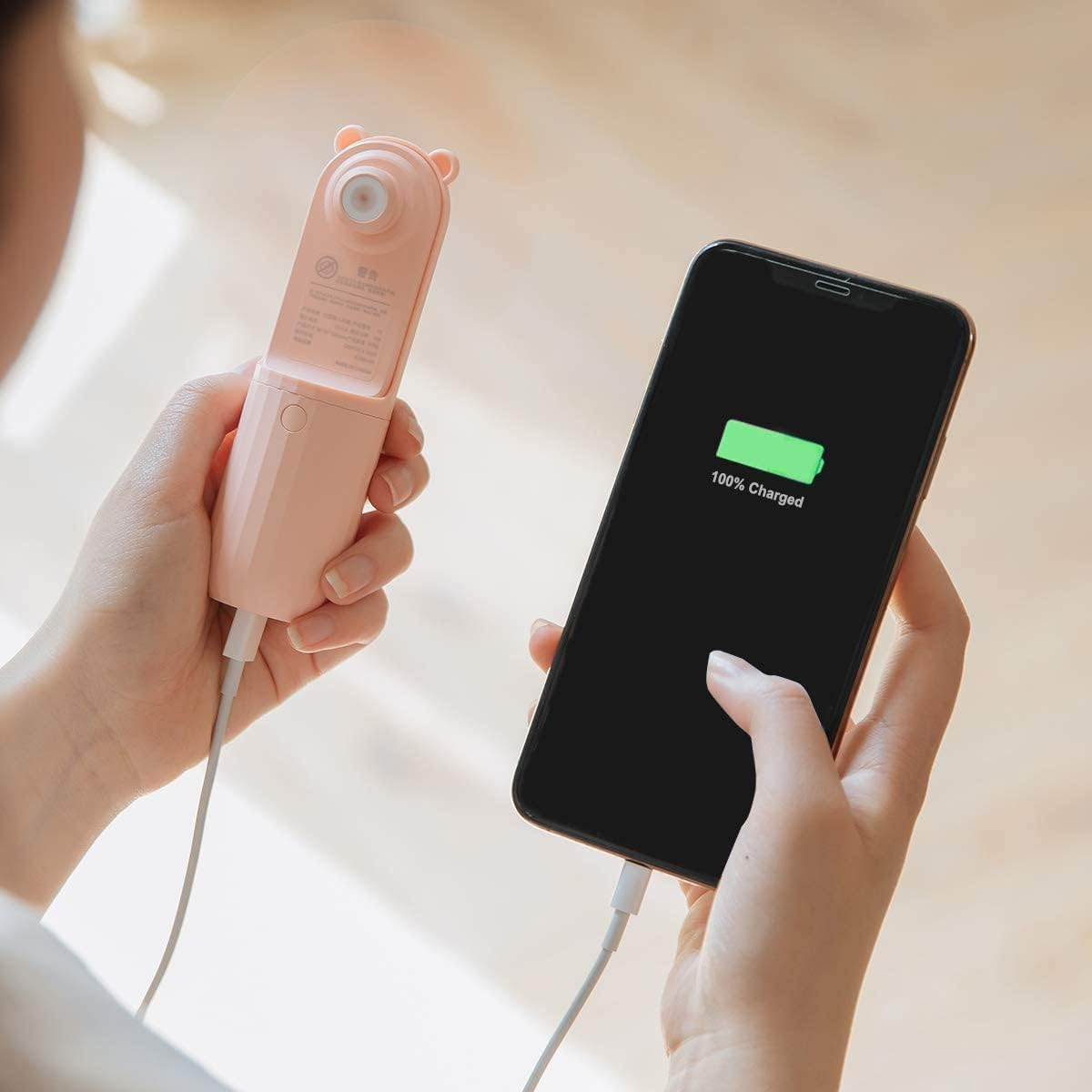 Eine Person lädt ein Smartphone mit einem kleinen rosa Lüfter auf.