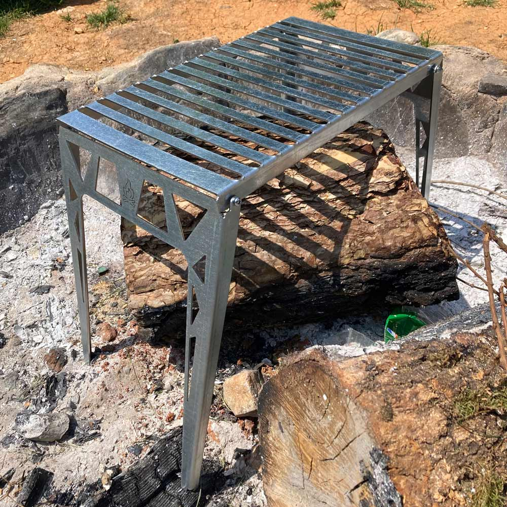 Kül içinde bir ateş çukurunda kütüğün üzerinde metal bir ızgara duruyor.