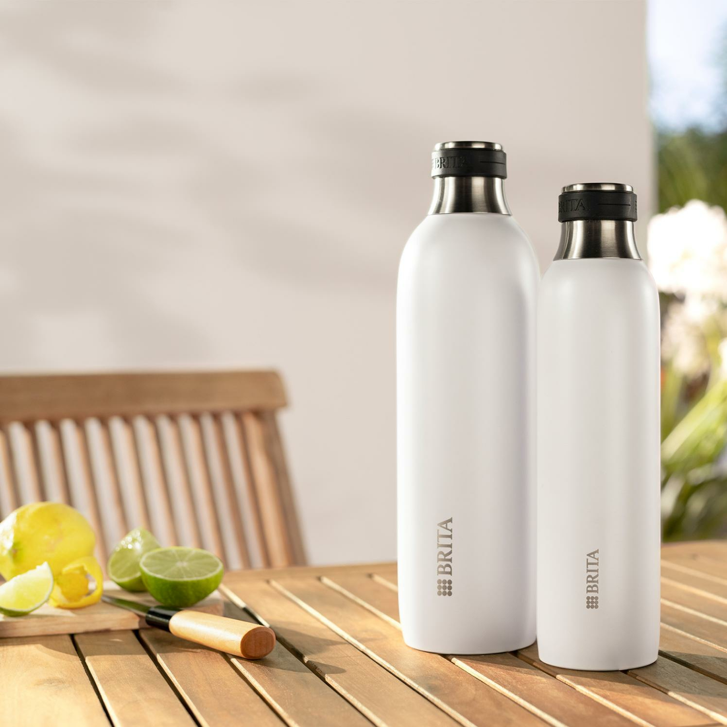 Zwei weiße Brita-Flaschen auf Holztisch mit Zitrusfrüchten und Messer.
