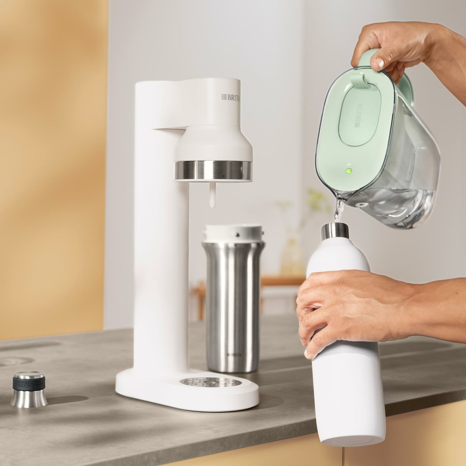 Eine Hand gießt Wasser von einem grünen Brita-Krug in eine weiße Flasche.