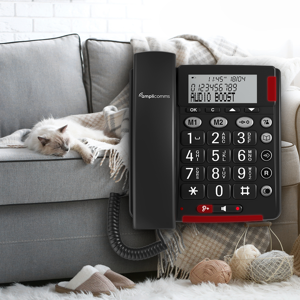 Un téléphone filaire à gros boutons est posé sur un canapé à côté d'un chat.