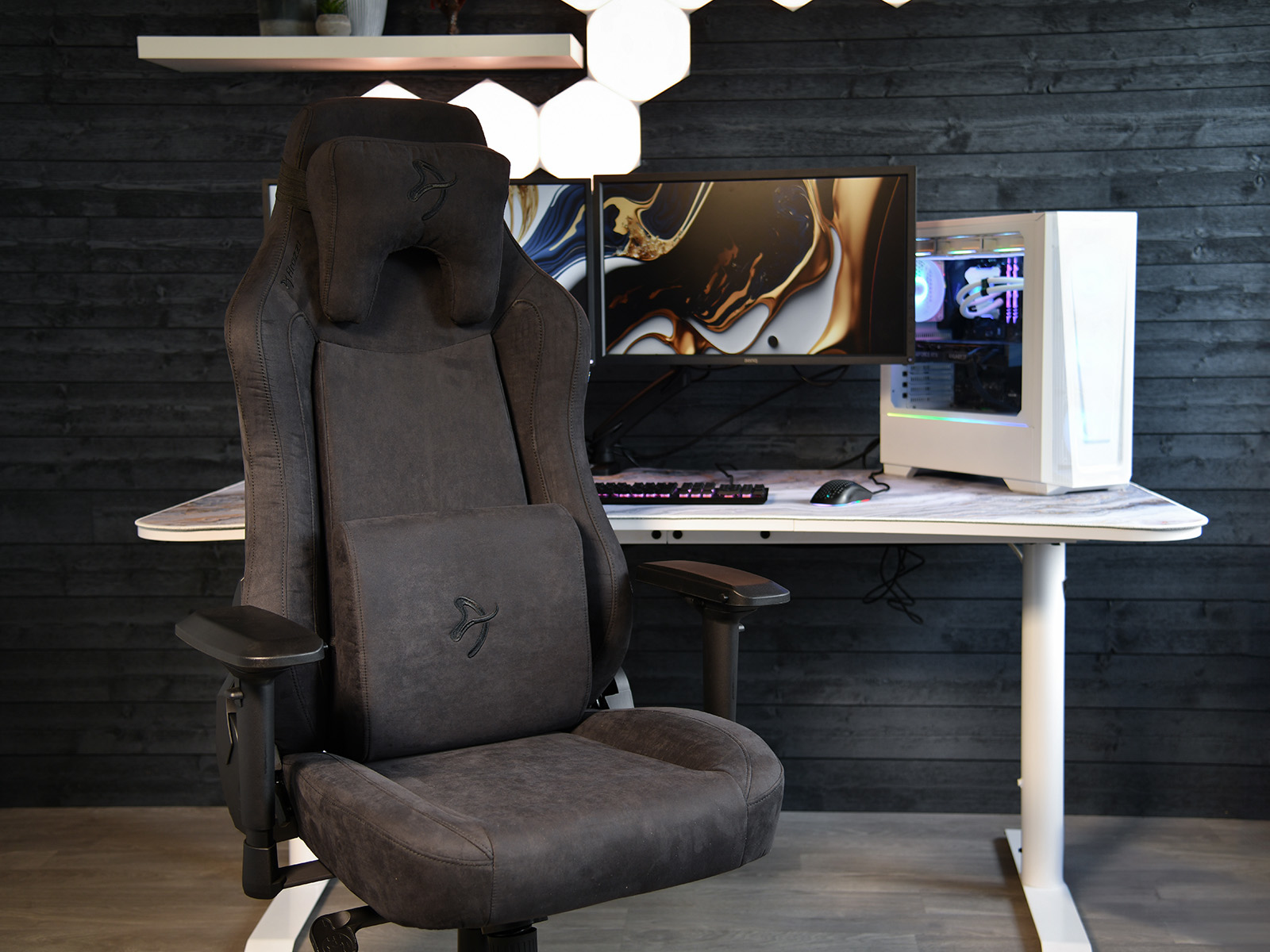 Een donkere gamestoel staat voor een bureau met twee monitoren en een pc.