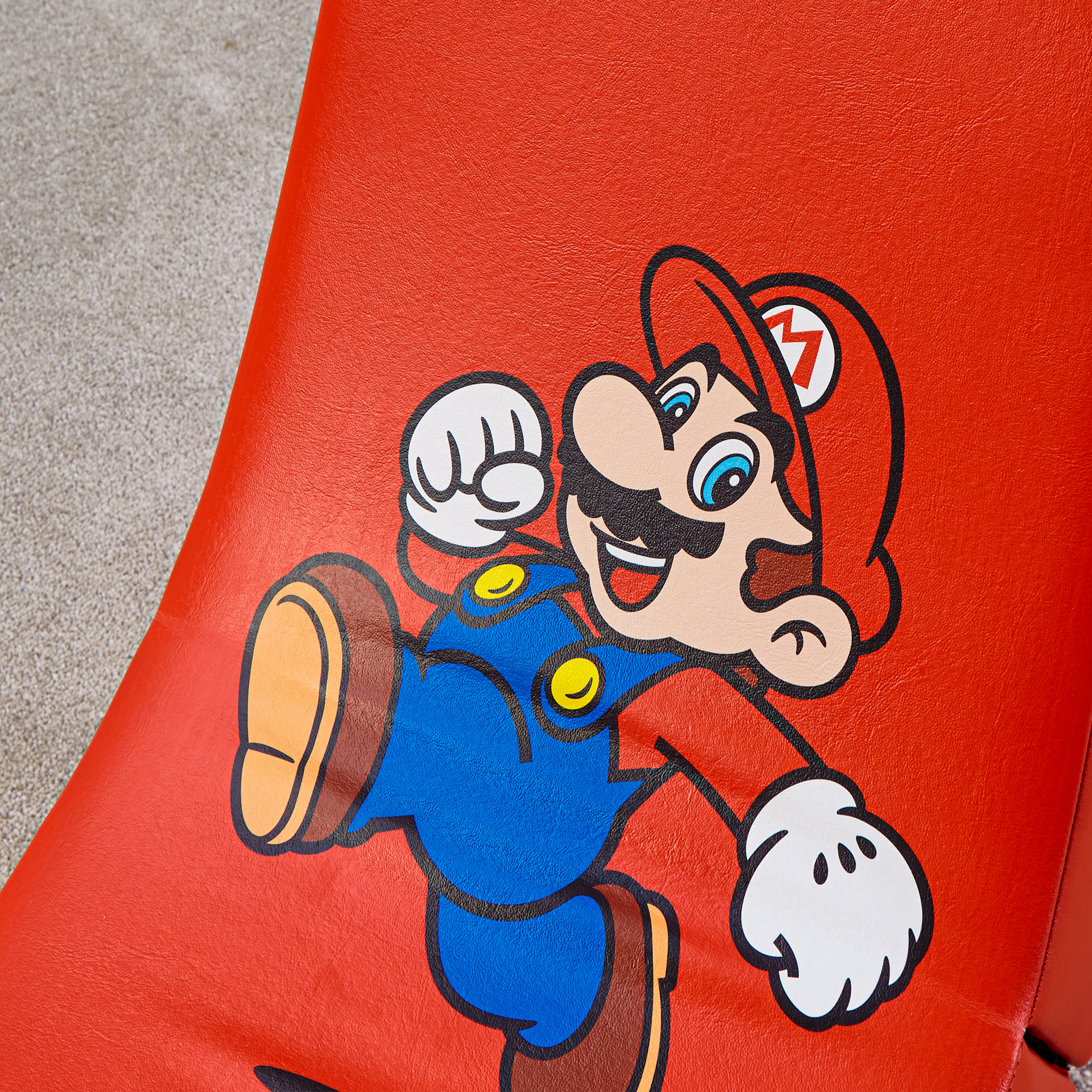 Zeigt Mario mit seinem roten Hut und blauer Latzhose auf rotem Hintergrund.