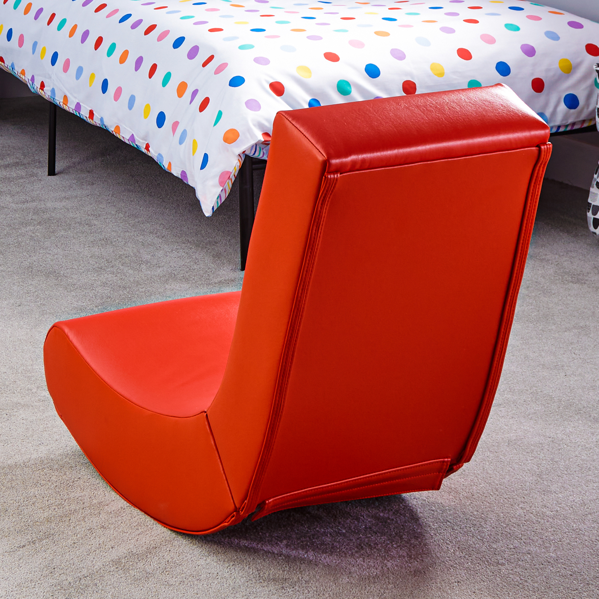 Ein orangeroter Sitzsack steht vor einem Bett mit bunter Tupfenbettwäsche.