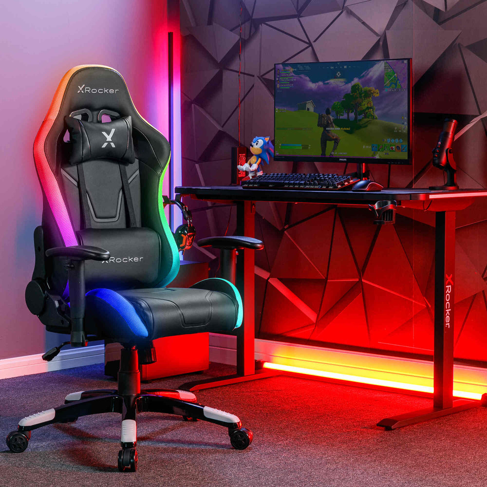 Ein Gaming-Stuhl und Schreibtisch mit RGB-Beleuchtung und einem Monitor, der ein Spiel anzeigt.