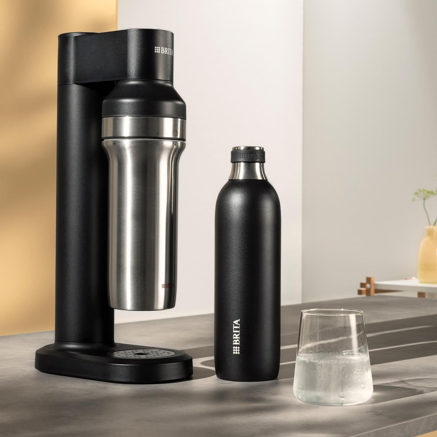 Schwarzer Brita Wassersprudler mit Edelstahlflasche, schwarzer Flasche und Wasserglas.