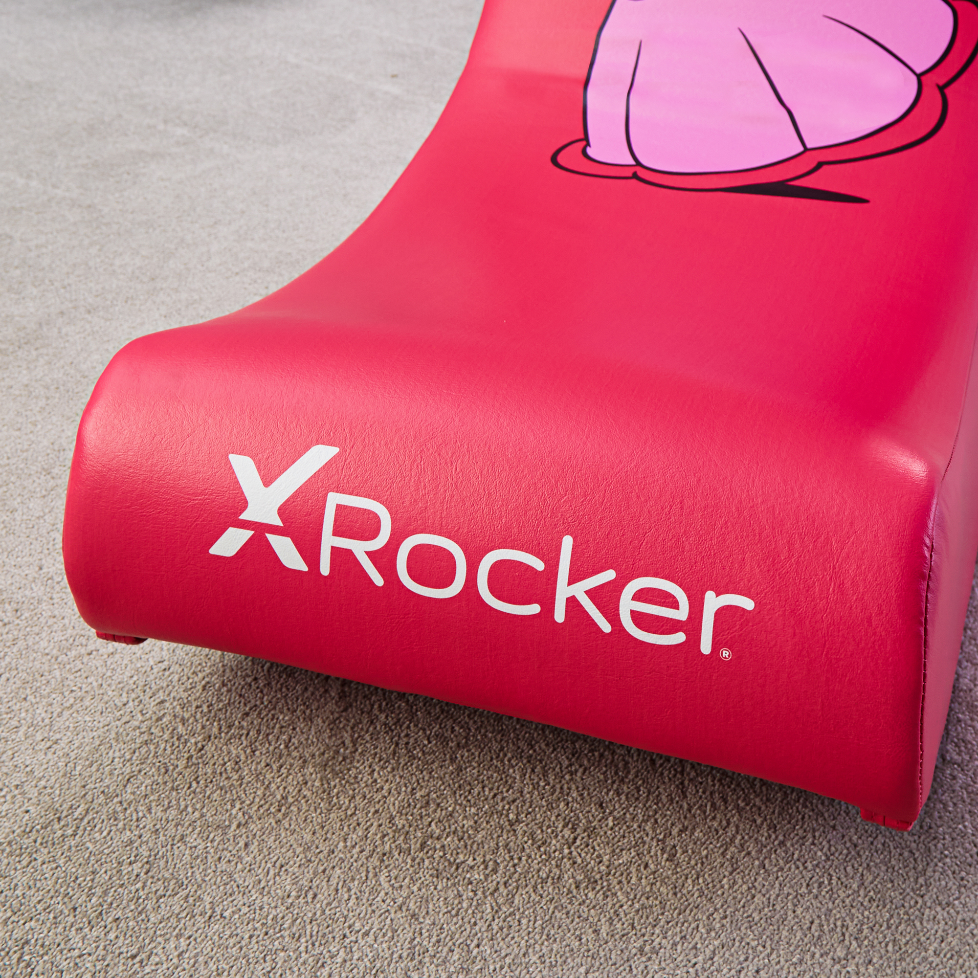 Rode X-Rocker gamestoel met roze stripfiguurdetail op grijs tapijt.