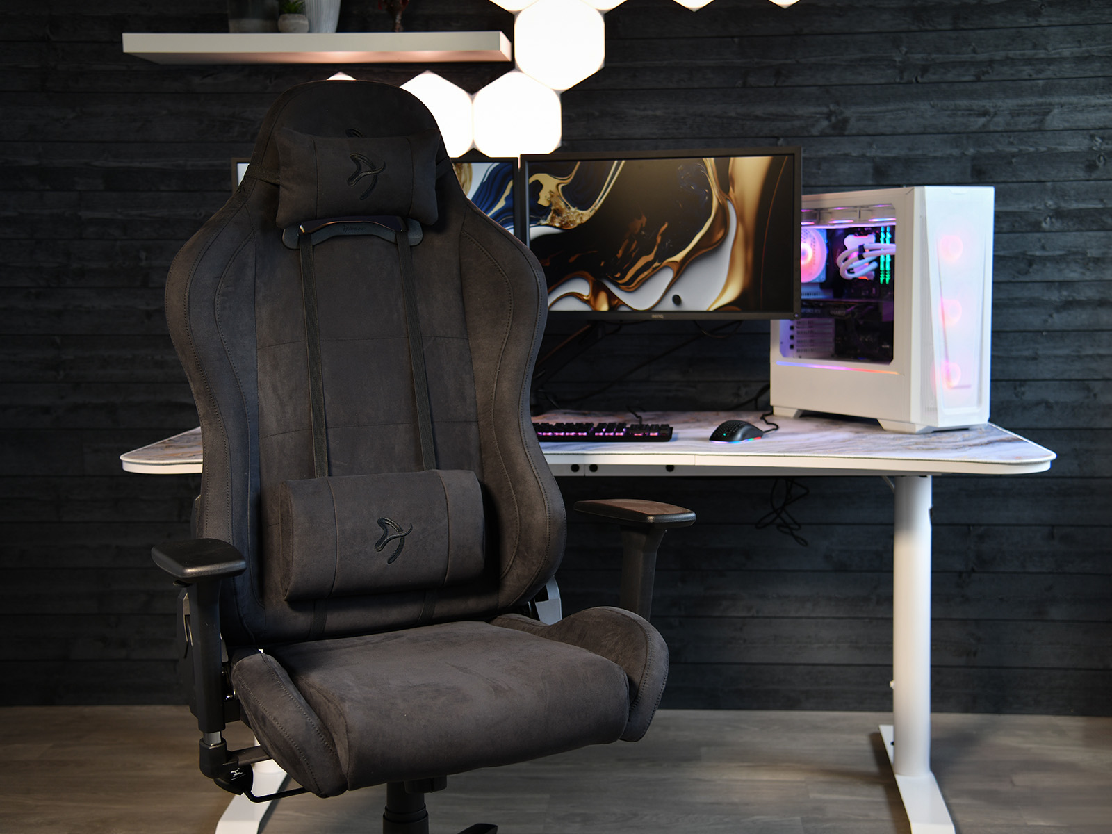 Een donkere gamestoel staat voor een bureau met computerapparatuur.