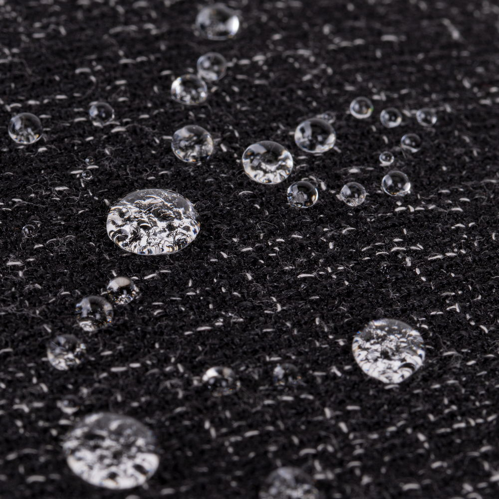 Gotas de agua sobre una tela oscura y texturizada con motas blancas.