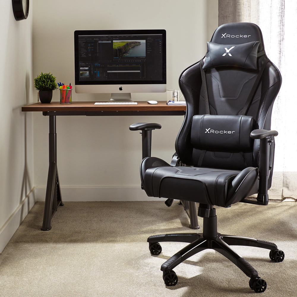Ein schwarzer X-Rocker Gaming-Stuhl steht vor einem Schreibtisch aus Holz mit einem Computer.
