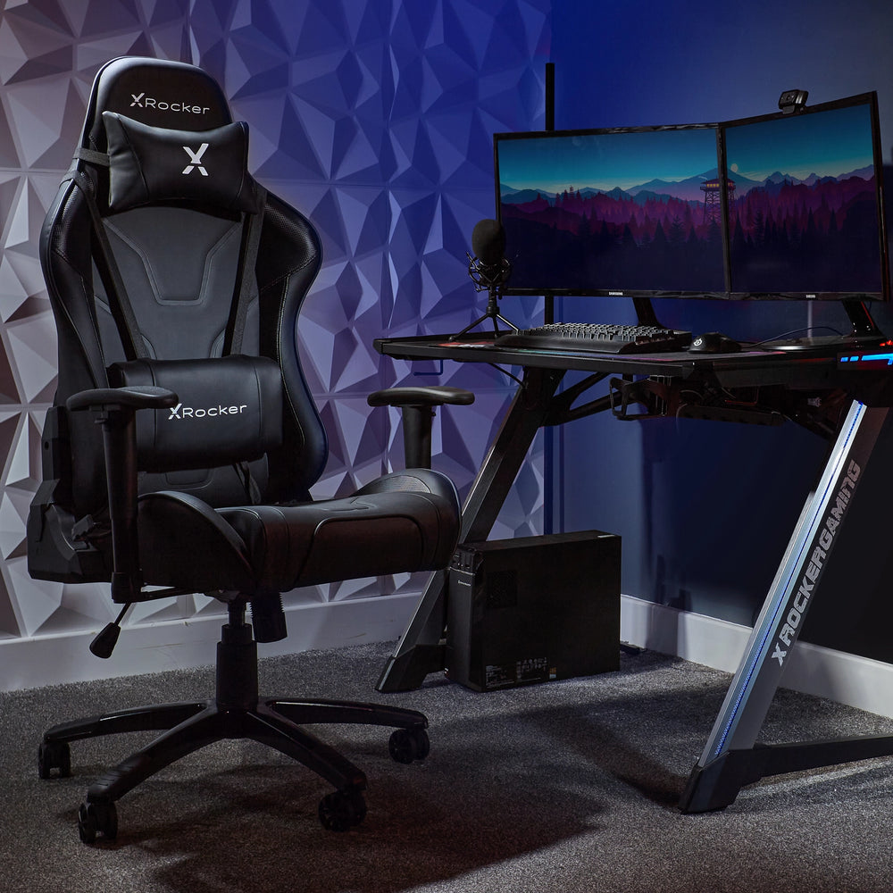 Ein schwarzer Gaming-Stuhl steht neben einem Schreibtisch mit zwei Monitoren.