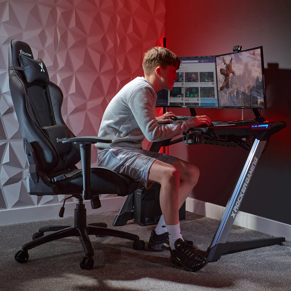 Ein Junge sitzt in einem Gaming-Stuhl vor einem Schreibtisch mit zwei Monitoren.
