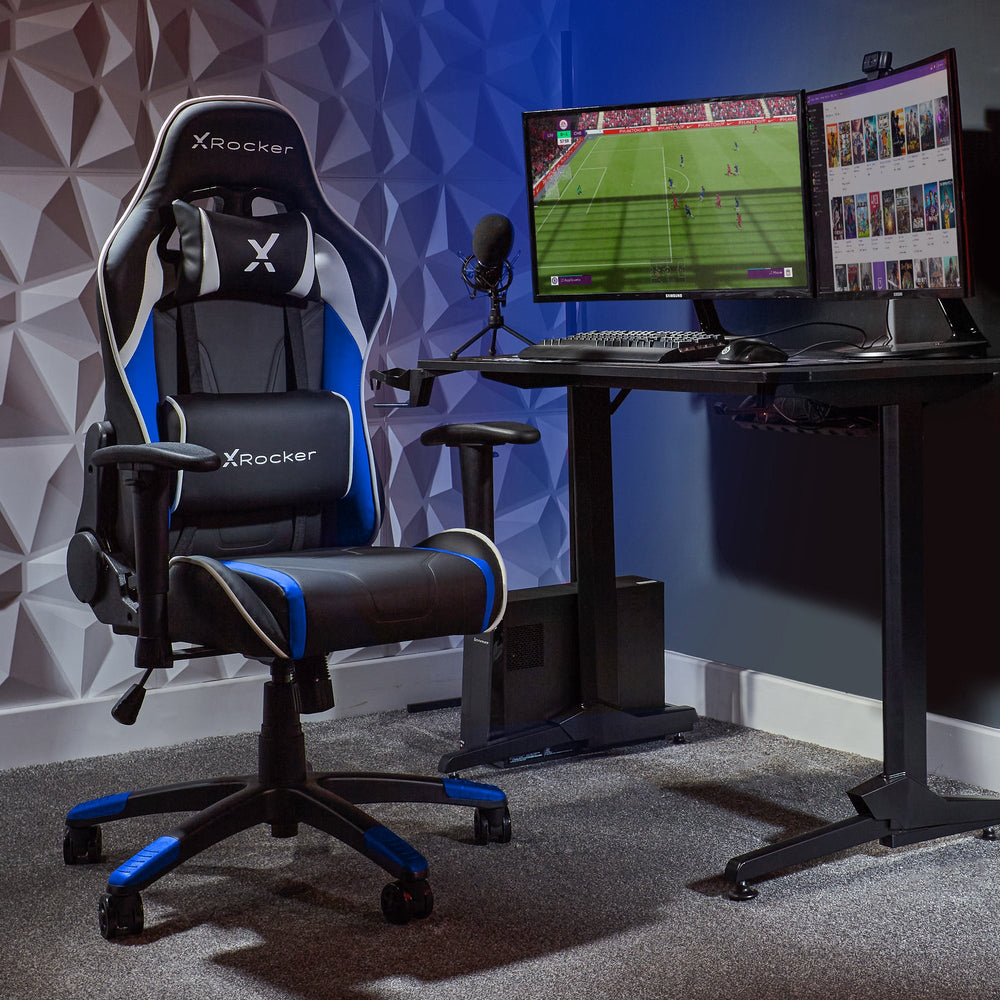 Ein schwarzer und blauer Gaming-Stuhl steht neben einem Schreibtisch mit zwei Monitoren, Tastatur, Maus und Mikrofon.