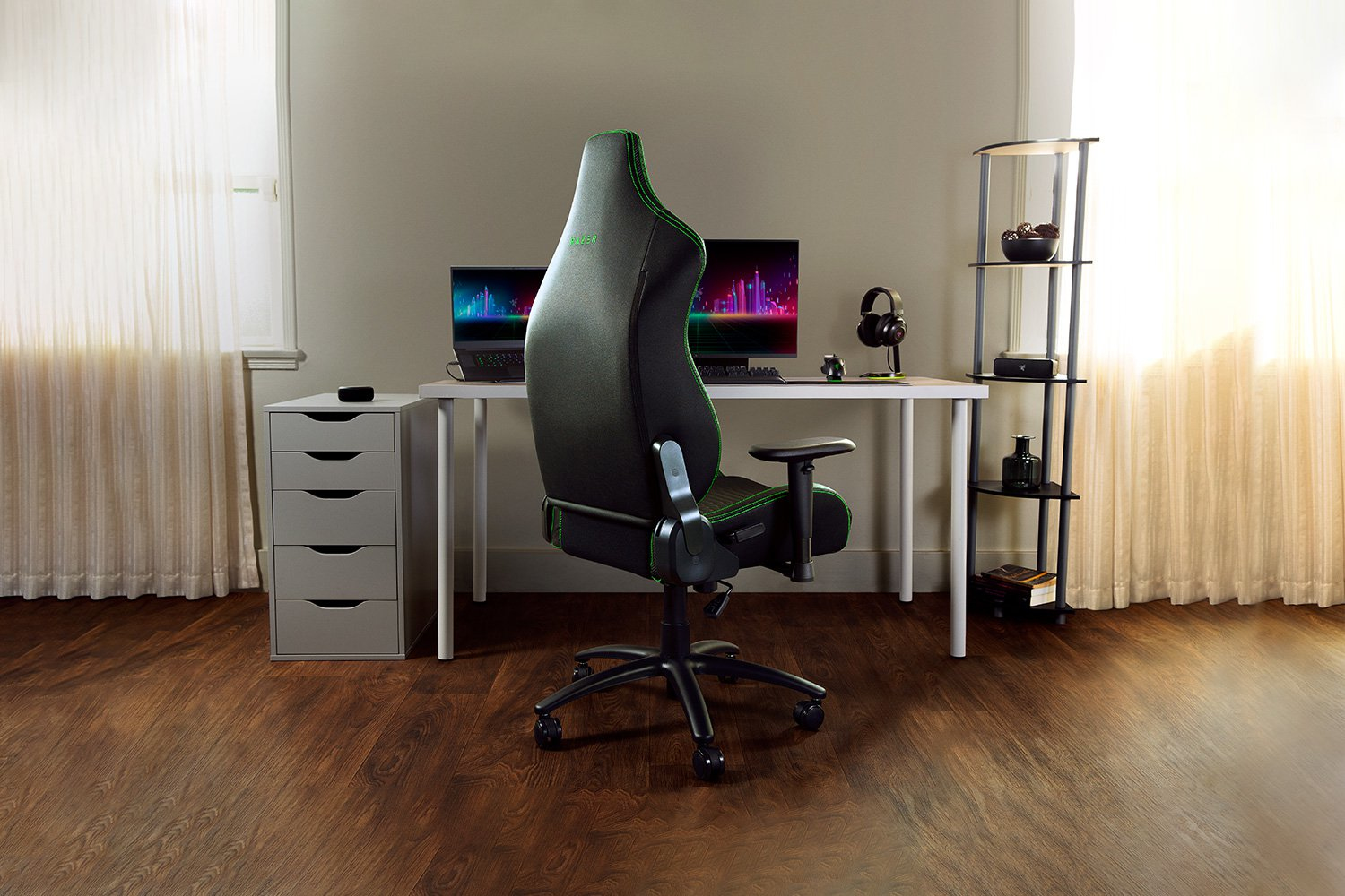 Sedia da gaming nera con bordi verdi in stanza con scrivania, laptop, monitor e mensola.