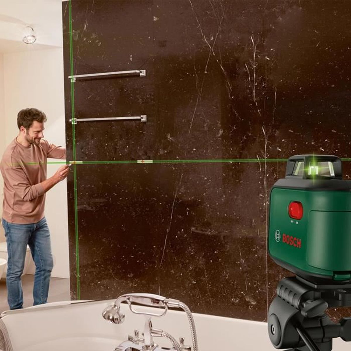 Mężczyzna wyrównuje poziomicę laserową na ciemnej ścianie, wanna na pierwszym planie.