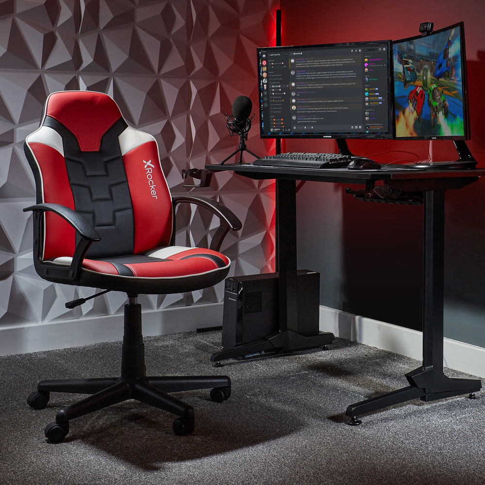 Ein roter, schwarzer und weißer Gaming-Stuhl steht neben einem Schreibtisch mit zwei Monitoren, Tastatur, Maus und Mikrofon.